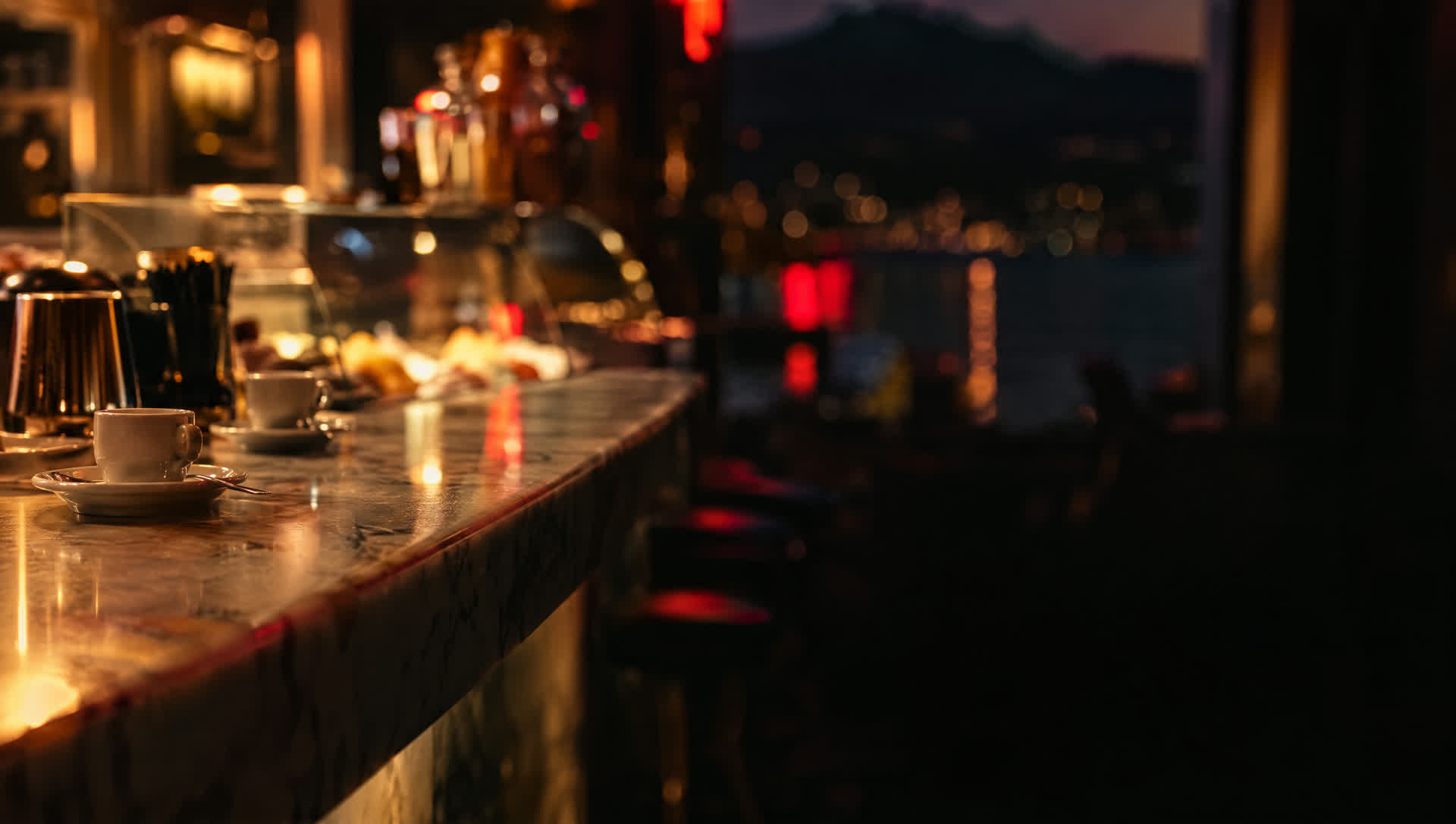 Banco in marmo di un bar la sera, con le tazzine da caffè e il lago dietro la vetrata