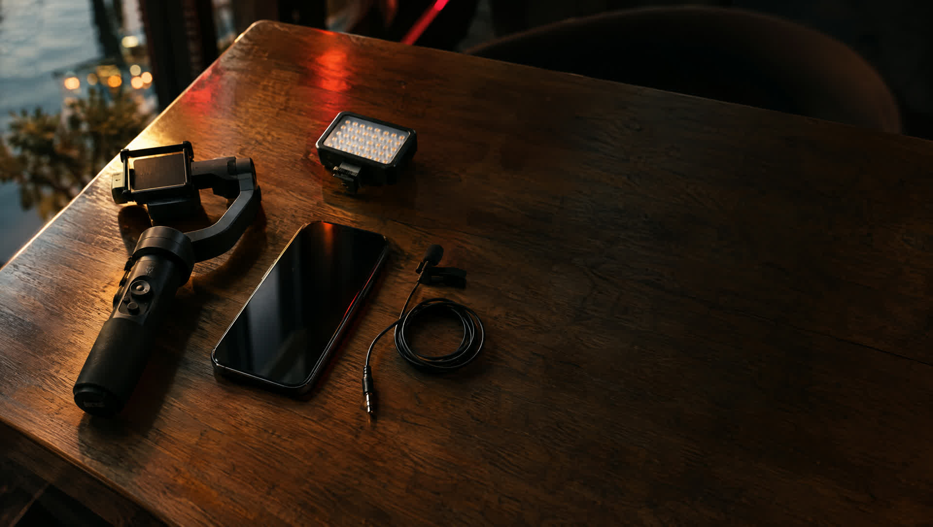 Attrezzatura per le riprese su un tavolo di legno: telefono, stabilizzatore, luce e microfono
