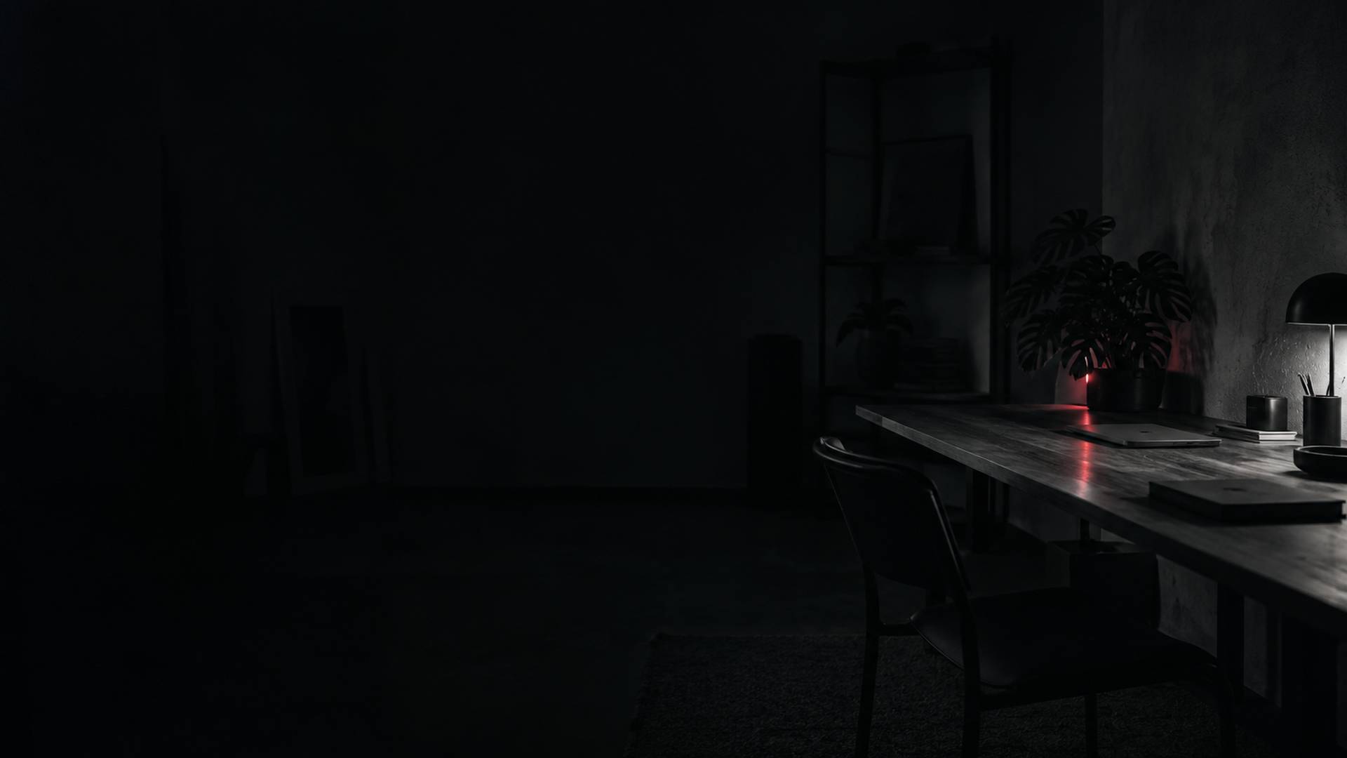 Ufficio in penombra con una lunga scrivania, una lampada e una pianta